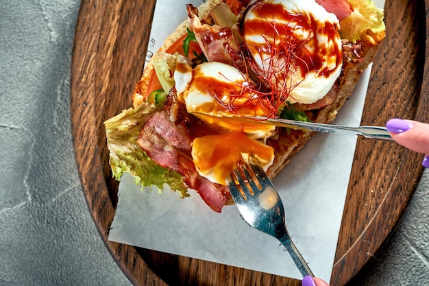 Ein Mädchen schneidet ein Sandwich mit Tomatenspeck und einem pochierten Ei zum Frühstück Betonhintergrund Hartes Licht