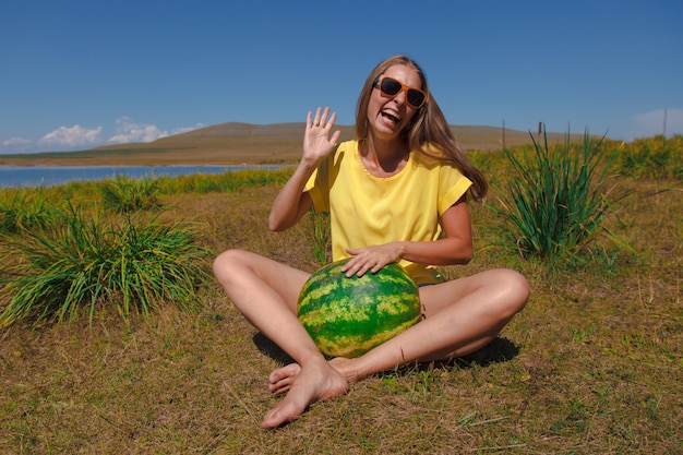 Ein Mädchen sitzt am Strand und hält eine Wassermelone. Reife der Sommerbeeren Fröhliche Emotionen und Stimmung. Picknick im Sommer.
