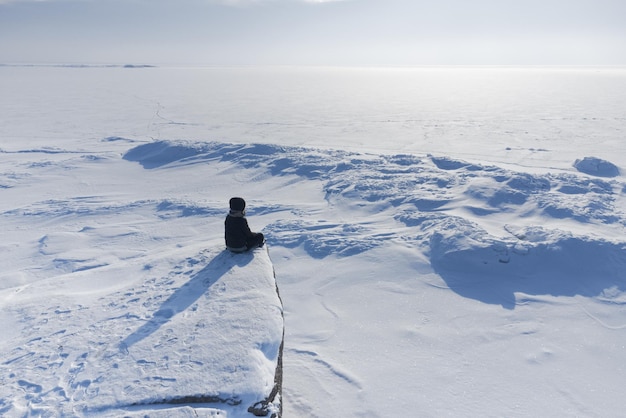 Ein Mädchen sitzt am Ufer eines gefrorenen Meeres und schaut in den Horizont