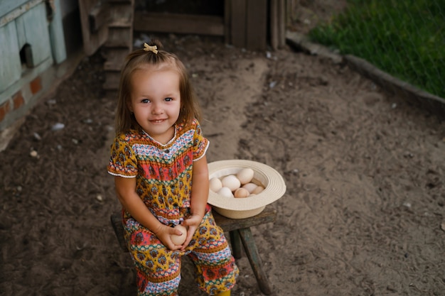 Ein Mädchen sitzt auf einem Stuhl in der Nähe des Hühnerstalls und hält ein Hühnerei in der Hand