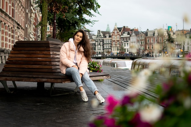 Ein Mädchen sitzt auf einer Bank in der Altstadt. Im Hintergrund ist die schöne Natur, Kanäle und Häuser von Amsterdam. Touristenurlaub.