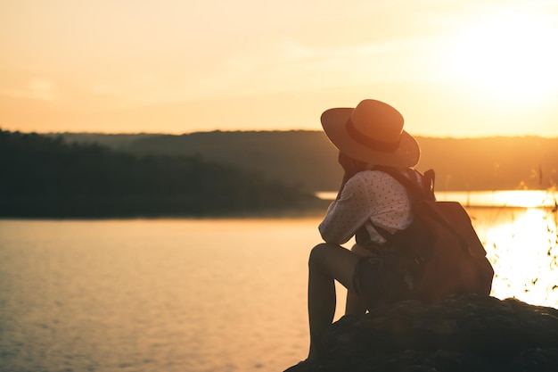 Foto ein mädchen sitzt bei sonnenuntergang auf einem felsen am see.