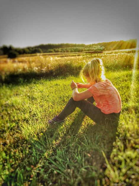 Ein Mädchen sitzt bei Sonnenuntergang auf einem grasbewachsenen Feld