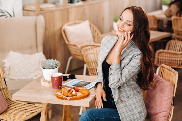 Ein Mädchen sitzt in einem Café und telefoniert, ein Mädchen in einem Café lächelt und brennt auf einem Smartphone, Süßigkeiten liegen auf dem Tisch