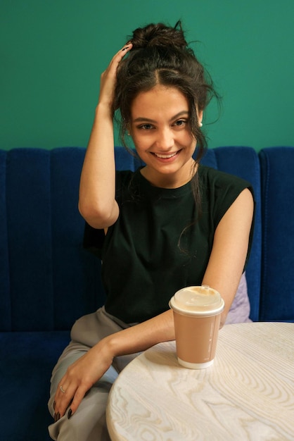 Ein Mädchen sitzt mit einem Glas Kaffee an einem Tisch in einem Café, schaut in die Kamera und lächelt