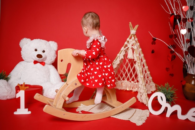 Ein Mädchen spielt auf einem kleinen Holzpferd Geburtstag 1 Jahr Roter Hintergrund für Foto