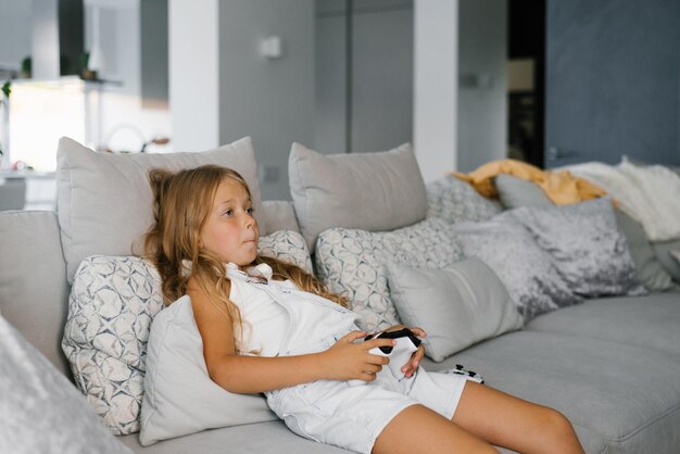 Ein Mädchen spielt aufmerksam ein Videospiel mit einer Spielkonsole, die auf der Couch sitzt