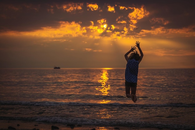 Ein Mädchen springt während des Sonnenuntergangs am Strand.