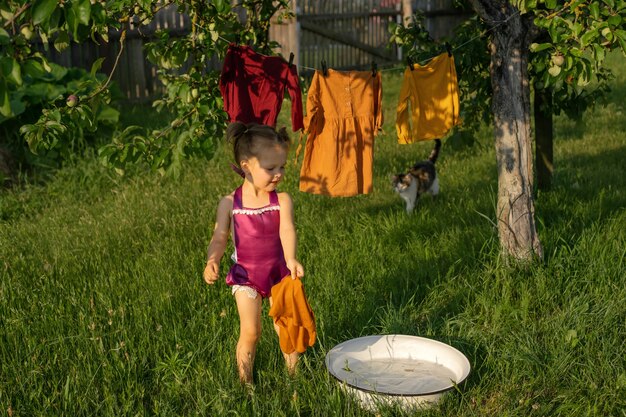 Ein Mädchen spritzt in ein Becken mit Seifenlauge, wäscht Kleidung und hängt Kleidung zum Trocknen auf