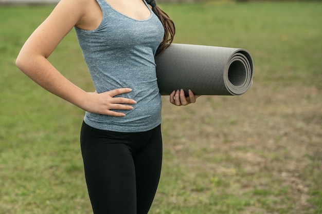 Foto ein mädchen steht mit einer zusammengerollten gymnastikmatte in den händen auf dem rasen.