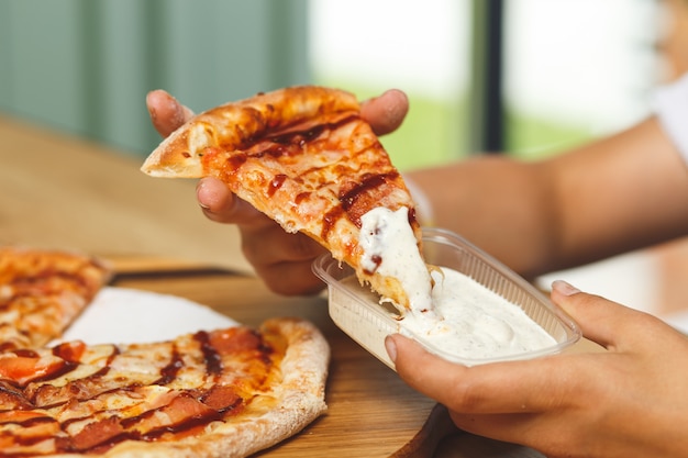 Ein Mädchen taucht ein Stück Pizza in Sauce in einen Plastikbehälter, bevor es es isst