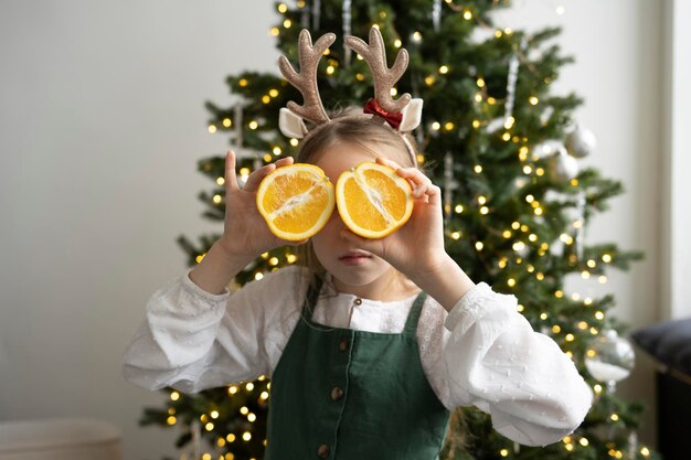 Ein Mädchen trägt eine grüne Schürze mit Geweih und einen Weihnachtsbaum hinter sich