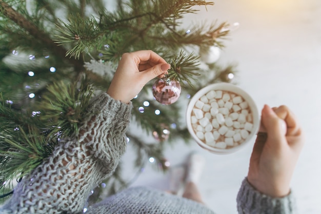 Ein Mädchen trinkt Kakao mit Eibisch und dekoriert einen Weihnachtsbaum.