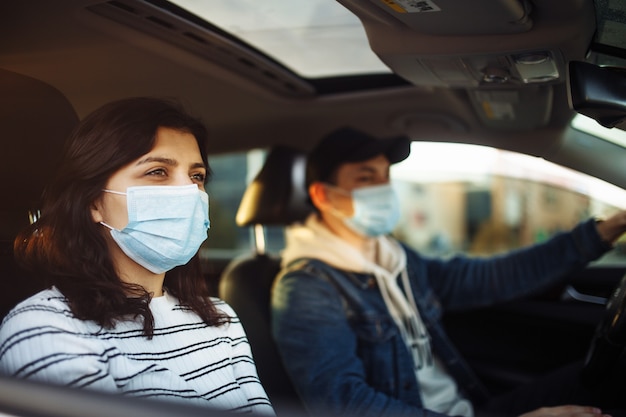 Ein Mädchen und ein Junge, die in einem Auto während der Coronavirus-Quarantäne fahren, die medizinische Masken tragen