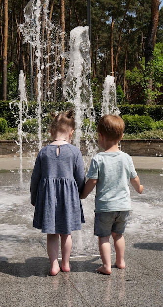 Ein Mädchen und ein Junge halten sich vor einem Brunnen auf einer Granitfliese im Park an den Händen