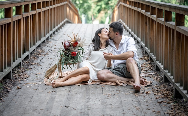 Ein Mädchen und ein junger Mann sitzen auf der Brücke und küssen sich, ein Date in der Natur, eine Liebesgeschichte.