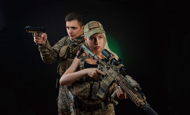 Ein Mädchen und ein Mann in Militäroveralls posieren mit einer Airsoft-Pistole auf dunklem Hintergrund