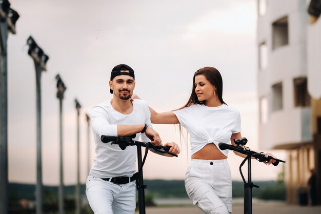 Ein Mädchen und ein Mann laufen mit Elektrorollern durch die Stadt, ein verliebtes Paar mit Rollern.