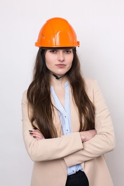 Ein Mädchenarchitekt in einem Anzug und einem orangefarbenen Bauhelm steht auf einem weißen Hintergrund.