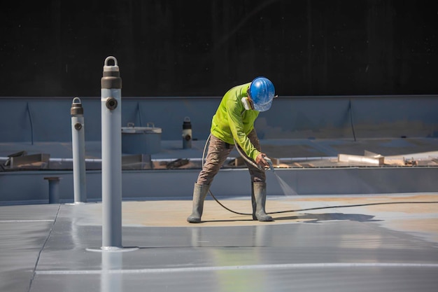 Ein männlicher Arbeiter, der eine industrielle Spritzpistole hält, die für die Oberfläche des Dachplattentanks auf der industriellen Lackierung und Beschichtung von Stahl verwendet wird