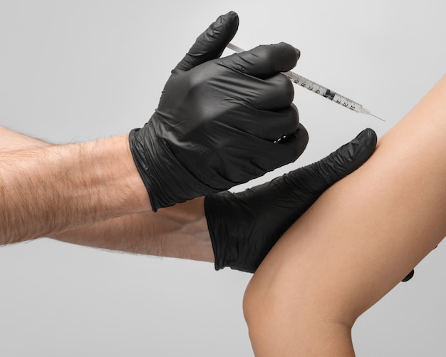 Ein männlicher Arzt, der schwarze Latexhandschuhe trägt, gibt dem Patienten die Impfung an der Schulter mit einer 1-ml-Einwegspritze aus der Nähe.