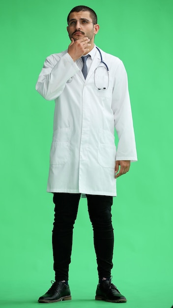 ein männlicher Arzt in einem weißen Mantel auf einem grünen Hintergrund lächelt in voller Länge