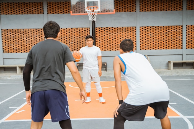 Ein männlicher Basketballspieler, der den Ball trägt, wird von zwei gegnerischen Spielern in Bereitschaft geblockt