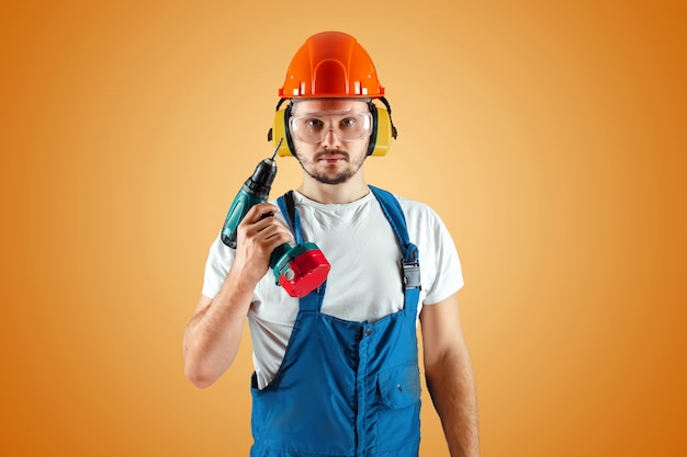 Ein männlicher Bauarbeiter in einem orangefarbenen Helm hält einen Schraubendreher auf einem orangefarbenen Hintergrund.