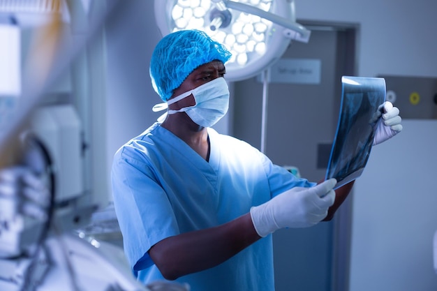 Ein männlicher Chirurg mit chirurgischer Maske untersucht Röntgenbilder im Operationssaal eines Krankenhauses