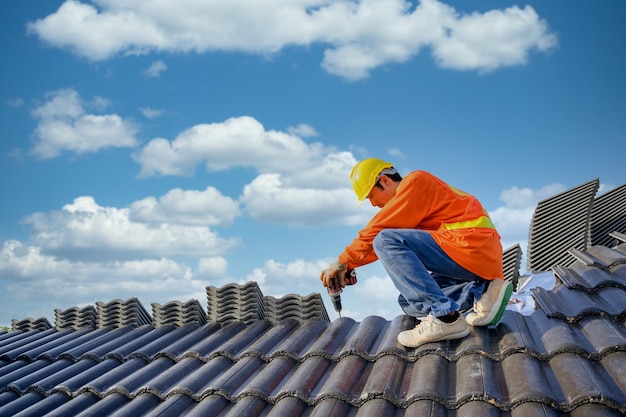 Ein männlicher Dachdecker arbeitet auf dem Dach eines Hauses Bauarbeiter reparieren das Dach eines Hauses mit Bohrern und Schrauben