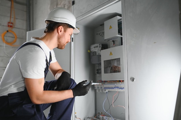 Ein männlicher Elektriker arbeitet an einem Schaltbrett mit einem elektrischen Verbindungskabel
