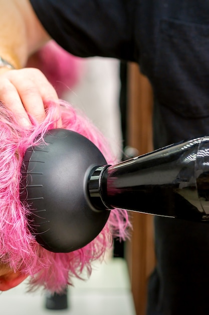 Ein männlicher Friseur, der in einem Schönheitssalon stilvolle rosa Haare der Kundin mit einem Fön trocknet