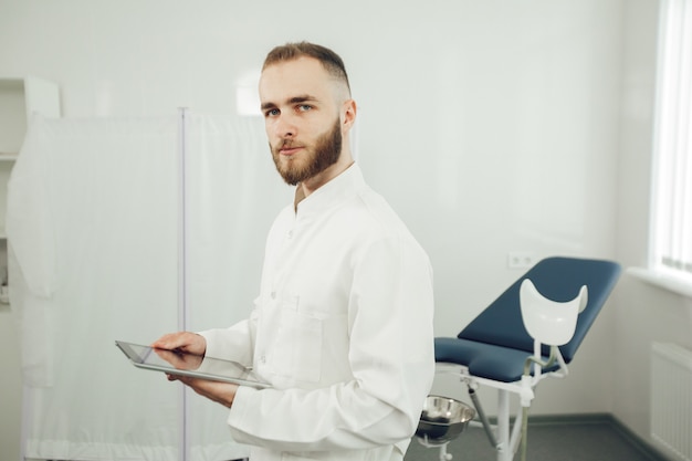 Ein männlicher Gynäkologe ist allein im Büro, hält ein Tablet in der Hand und schaut in die Kamera. Das Konzept der modernen Medizin