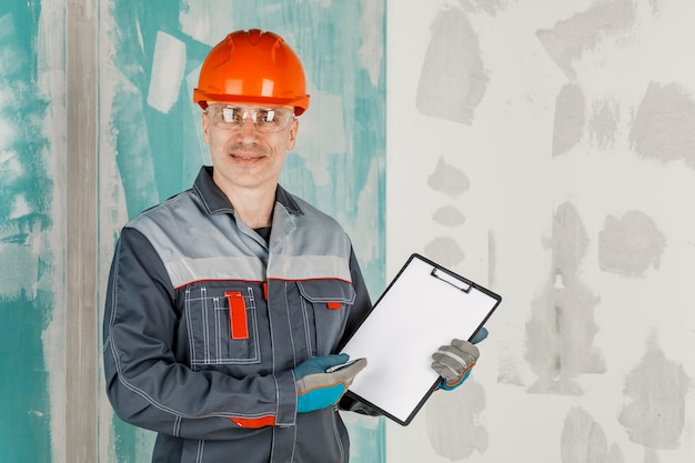 Ein männlicher Ingenieur, ein Bauarbeiter mit Schutzhelm und Brille, schreibt auf ein Tablet Das Konzept der Renovierung und des Baus