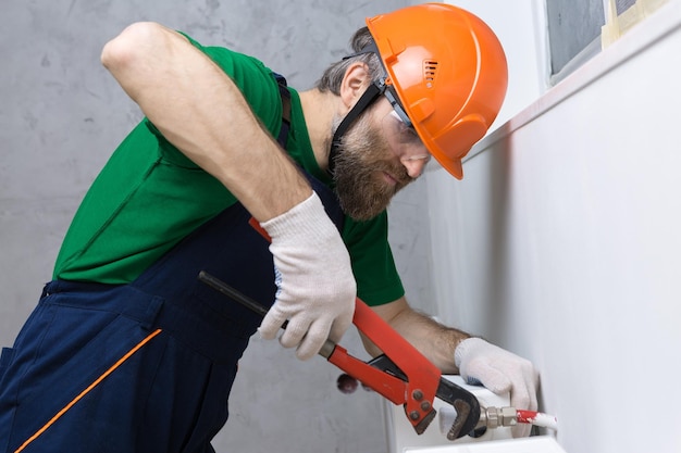 Ein männlicher Klempner installiert einen Heizkörper in der Heizungsanlage einer Wohnung Typ in Overall und Gasschlüssel