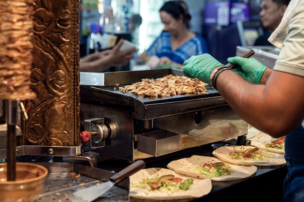 Ein männlicher Koch bereitet auf der Straße einen Fleisch-Shawarma zu, er legt gebratenes Fleisch in Tortillas, die Köche behandschuht ...