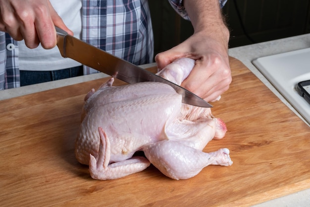 Ein männlicher Koch schneidet frisches hausgemachtes Hähnchen auf einem Holzbrett Das Hähnchen in teilweise Brustflügelbeinen schlachten