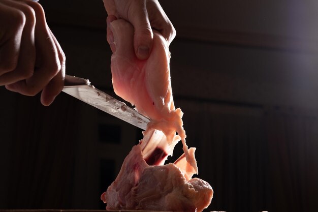 Ein männlicher Koch schneidet frisches hausgemachtes Hähnchen auf einem Holzbrett Das Hähnchen in teilweise Brustflügelbeinen schlachten