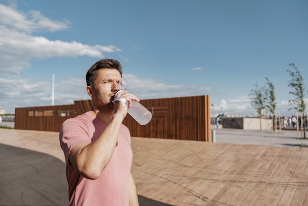 Ein männlicher Läufer trinkt sauberes Wasser aus einer Sportflasche. Ruhe beim Fitness auf der Straße verbraucht