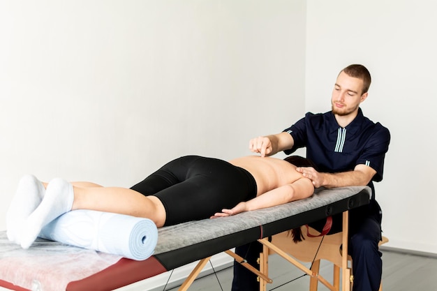 Foto ein männlicher massagetherapeut in einem blauen anzug macht eine sportmassage zu einer rückenschmerzbehandlung einer frau