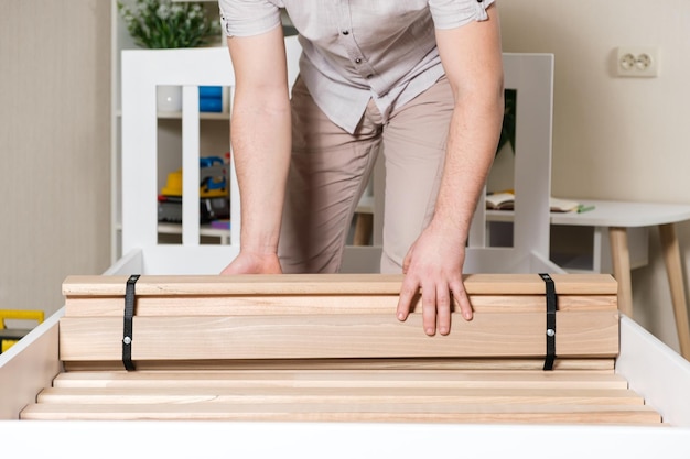 Ein männlicher Möbelmonteur legt Holzlatten auf einem neuen weißen Bett aus