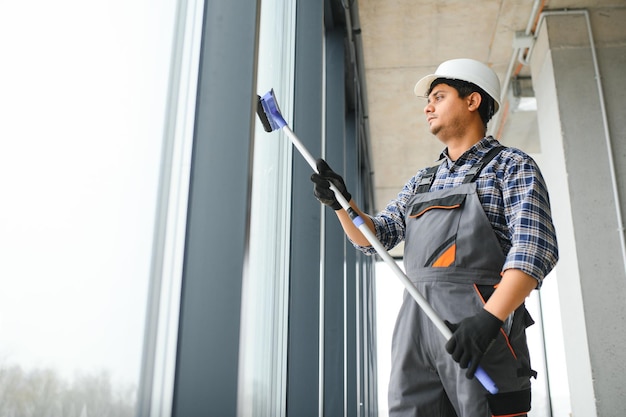 Ein männlicher professioneller Reinigungsarbeiter in Overall reinigt die Fenster und Schaufenster