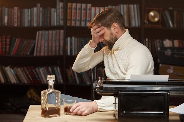 Ein männlicher Schriftsteller bedeckte seine Augen mit der Hand, während er an einer Schreibmaschine saß