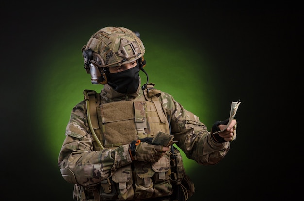 Ein männlicher Soldat in Militärkleidung mit einer Waffe auf dunklem Hintergrund mit Geld