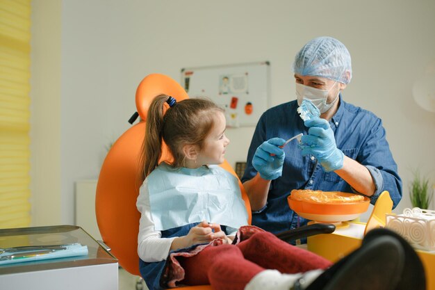 Ein männlicher Zahnarzt bringt einem kleinen Mädchen bei, wie man sich mit einer Zahnbürste die Zähne richtig putzt