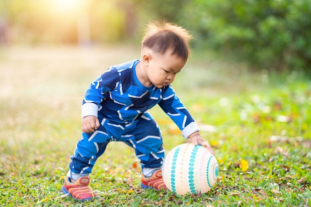 Ein männliches asiatisches kind, das im hinterhof im freien einen fußball hält und damit spielt