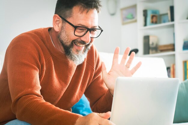 Ein Mann allein zu Hause sitzt auf dem Sofa und macht einen Videoanruf mit Laptop und Internetverbindung Konzept der Fernarbeit und Fernanrufe online Reife männliche Menschen und Technologie Innen-Freizeitaktivität