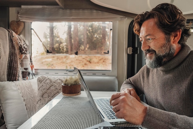 Ein Mann arbeitet am Laptop in einem Wohnmobil, das am Schreibtischtisch sitzt