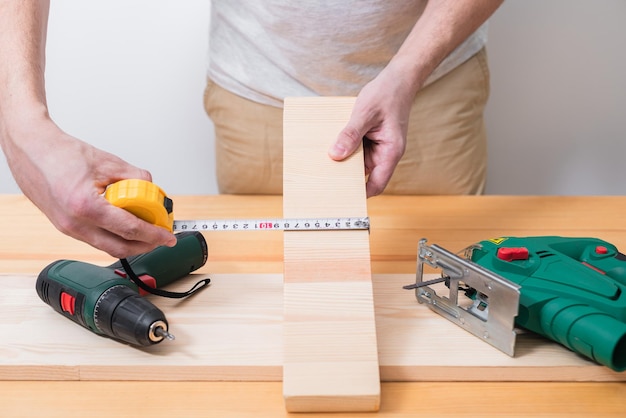 Ein Mann arbeitet mit einer Stichsäge und einem Schraubendreher auf einem Holztisch mit und ohne Handschuhe misst auch mit einem Maßband