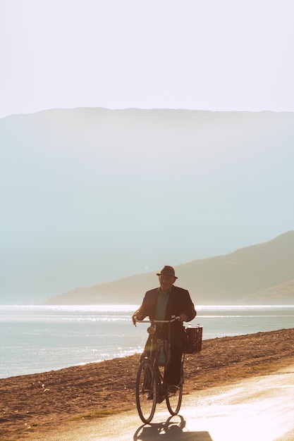 Ein Mann auf einem Fahrrad fährt an einem Strand mit Bergen im Hintergrund entlang.